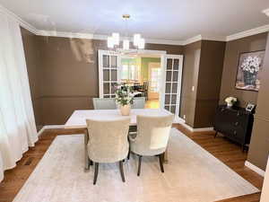 Dining room with wood finished floors, crown molding, a chandelier, and french doors