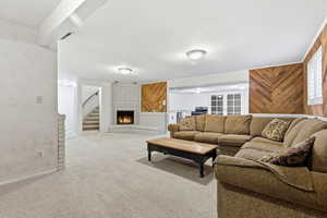 Living area featuring a fireplace, light carpet, wooden walls, and stairs