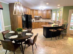 Kitchen featuring decorative backsplash, a breakfast bar, brown cabinets, black appliances, and a peninsula
