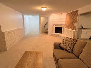Living area with a brick fireplace, light carpet, a textured ceiling, and stairway