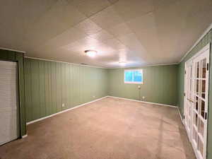Carpeted empty room with wood walls and french doors