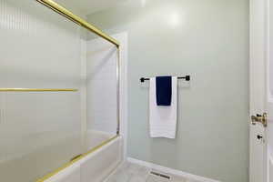 Full bath featuring light tile patterned flooring and bath / shower combo with glass door