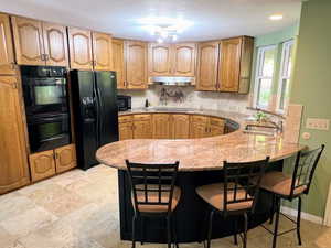 Kitchen featuring a kitchen bar, tasteful backsplash, black appliances, and light stone countertops