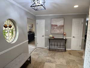 Foyer featuring ornamental molding, a chandelier, light stone finish floors, and recessed lighting