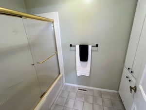Full bathroom featuring combined bath / shower with glass door and light tile patterned floors
