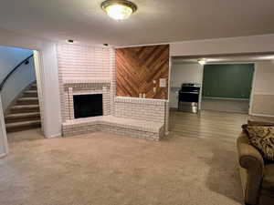 Living room with a textured ceiling, light carpet, a fireplace, and wood walls