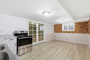 Kitchen with stainless steel range with electric stovetop, a textured ceiling, wood walls, light wood finished floors, and white cabinets