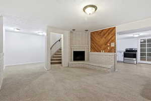 Unfurnished living room with a brick fireplace, light carpet, and a textured ceiling