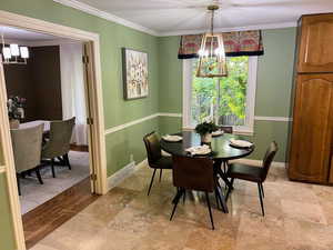 Dining room featuring a chandelier, crown molding, and light stone finish floors