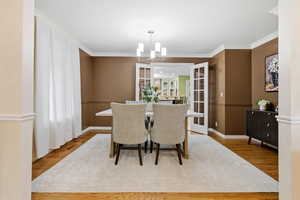 Dining area with wood finished floors, a chandelier, ornamental molding, and french doors