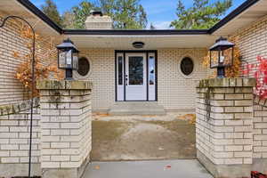 Entrance to property with a chimney, brick siding, and a patio area