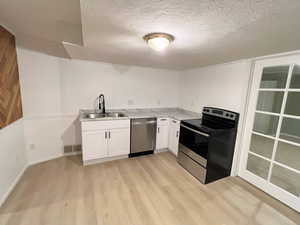 Kitchen featuring appliances with stainless steel finishes, light countertops, white cabinets, light wood finished floors, and a textured ceiling