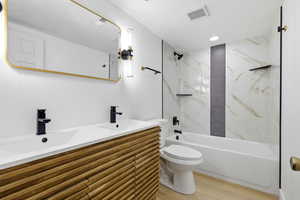 Bathroom featuring double vanity, a combined bath / shower with marble appearance, light wood-type flooring, and recessed lighting