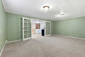 Empty room with french doors, wooden walls, and carpet floors