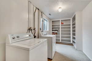 Laundry area with a textured ceiling, light colored carpet, and washing machine and dryer