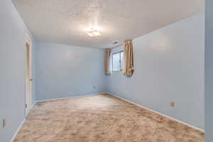 Carpeted empty room with a textured ceiling and baseboards