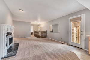 Unfurnished living room featuring light colored carpet, a fireplace with flush hearth, and light tile patterned flooring