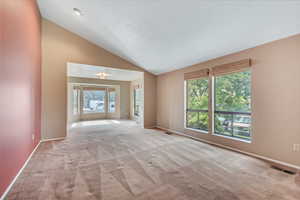 Carpeted empty room with high vaulted ceiling and baseboards