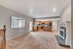 Kitchen featuring light colored carpet, light countertops, a center island, a fireplace with flush hearth, and appliances with stainless steel finishes