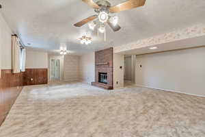 Unfurnished living room featuring light colored carpet, wallpapered walls, ceiling fan, a brick fireplace, and a textured ceiling