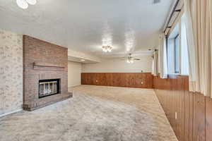 Unfurnished living room with wood walls, a fireplace, carpet floors, a ceiling fan, and a textured ceiling