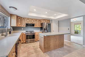 Kitchen featuring appliances with stainless steel finishes, a kitchen island, a tray ceiling, recessed lighting, and light tile patterned flooring