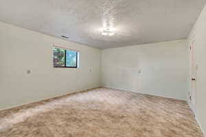 Empty room with light carpet and a textured ceiling