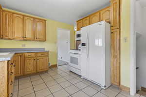 Kitchen with white appliances, light tile patterned floors, and light countertops