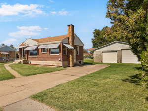Bungalow with an outbuilding, a front lawn, brick siding, a chimney, and a detached garage