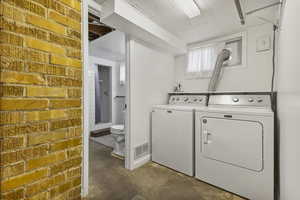 Laundry room featuring concrete flooring, independent washer and dryer, and brick wall