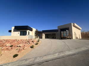 Contemporary house with stucco siding, concrete driveway, roof mounted solar panels, and an attached garage