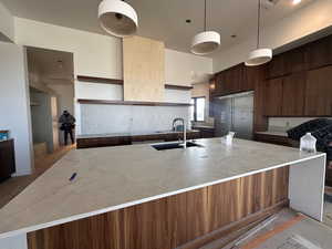 Kitchen featuring light stone countertops, dark wood finish cabinetry, high end refrigerator, a large island, and decorative light fixtures