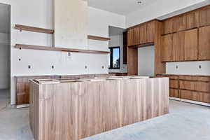 Kitchen featuring open shelves, wood finish cabinetry, unfinished concrete flooring, and a kitchen island