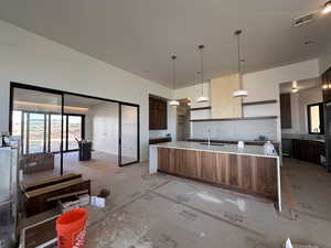 Kitchen with pendant lighting, modern cabinets, a large island, backsplash, and light stone counters