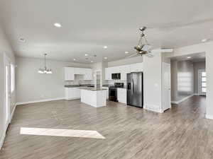 Kitchen featuring a chandelier, white cabinets, open floor plan, stainless steel appliances, and decorative light fixtures