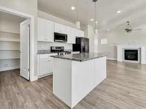 Kitchen featuring dark stone counters, white cabinets, pendant lighting, stainless steel appliances, and a kitchen island