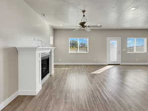 Unfurnished living room featuring a textured ceiling, light wood-style floors, a glass covered fireplace, recessed lighting, and a ceiling fan