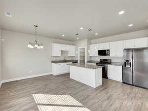 Kitchen with appliances with stainless steel finishes, pendant lighting, white cabinetry, dark stone counters, and a chandelier