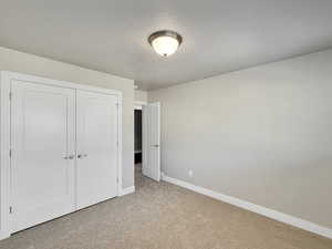 Unfurnished bedroom featuring light carpet, a textured ceiling, and a closet