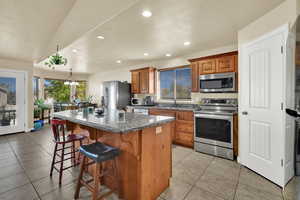 Kitchen with stainless steel appliances, a kitchen island, a breakfast bar, brown cabinets, and recessed lighting