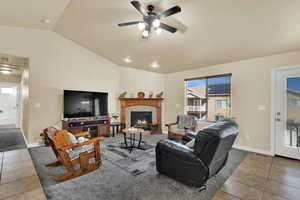 Tiled living room with vaulted ceiling, a fireplace, and a ceiling fan