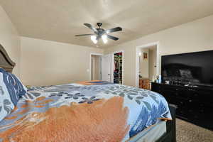 Carpeted bedroom with a ceiling fan, a spacious closet, and a textured ceiling