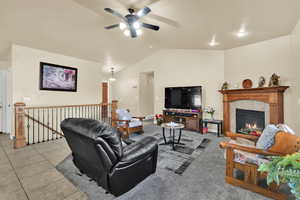 Living area with vaulted ceiling, a tile fireplace, ceiling fan, and light carpet