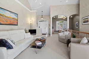 Carpeted living area with ornate columns, a towering ceiling, arched walkways, and recessed lighting