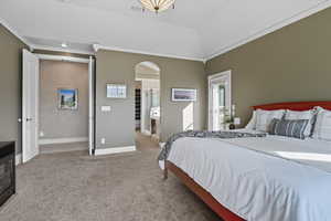 Primary Bedroom featuring light colored carpet, crown molding, arched walkways, and ensuite bathroom