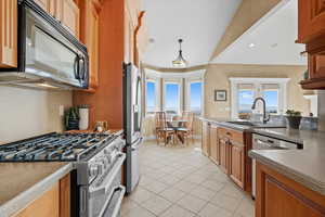 Kitchen featuring appliances with stainless steel finishes, decorative light fixtures, light tile patterned flooring, brown cabinets, and a peninsula