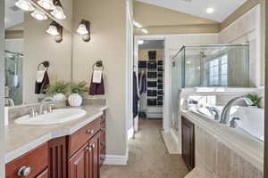 Full bathroom featuring a walk in closet, vanity, a shower stall, a bath, and vaulted ceiling