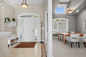 Entryway with ornate columns, light tile patterned flooring, a towering ceiling, a chandelier, and light colored carpet