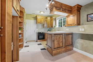 Kitchen with a peninsula, brown cabinets, light tile patterned flooring, black electric range, and light colored carpet