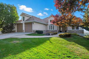 View of front facade with stucco siding, stone siding, driveway, a front lawn, and a garage